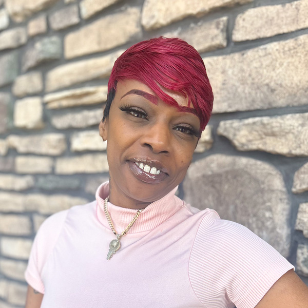 Tomesha Fairley, Memory Care Director at Vitalia Highland Heights, smiles in front of a stone wall while wearing a light pink top and gold key necklace.