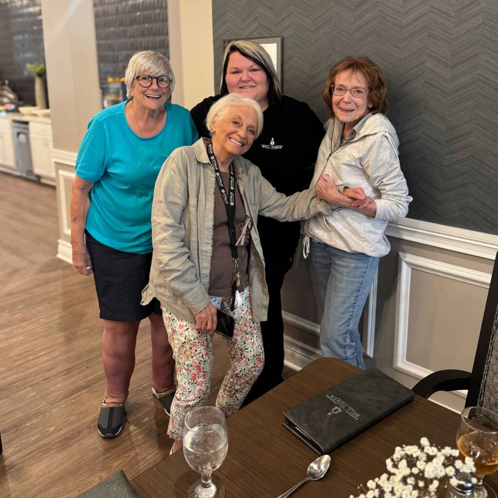 Culinary team member enjoys time with three senior residents, sharing laughter and camaraderie in the dining area after a community meal.