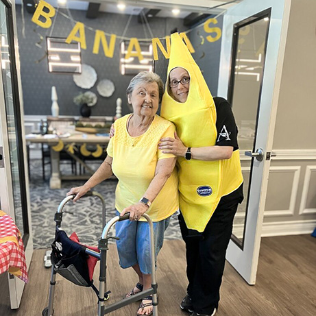 A team member in a banana costume smiles alongside a senior woman dressed in yellow during a banana-themed Wellness event.