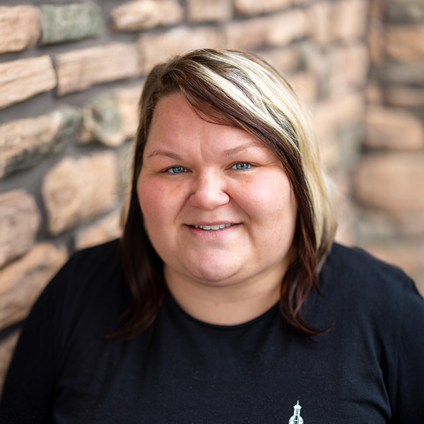 Stephanie Snyder, Culinary Director at Vitalia Highland Heights, smiling warmly while standing beside a tan stone wall and wearing a black top.