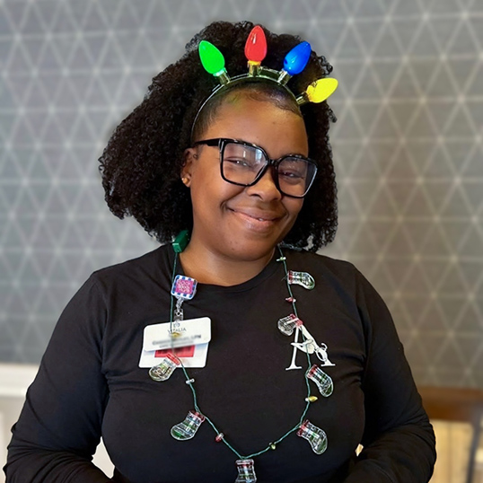 A woman on the Vitalia Highland Heights team smiles, wearing a festive crown of Christmas lights.