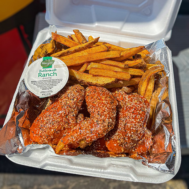 A container of fresh, hot food from a local businesses, featuring sauced and seasoned chicken wings, a heaping portion of fries, and a side of ranch dressing.
