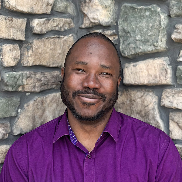 Fred Kope, Business Office Director at Vitalia Highland Heights, smiling in a professional headshot with a purple button-down shirt and a stone wall background.