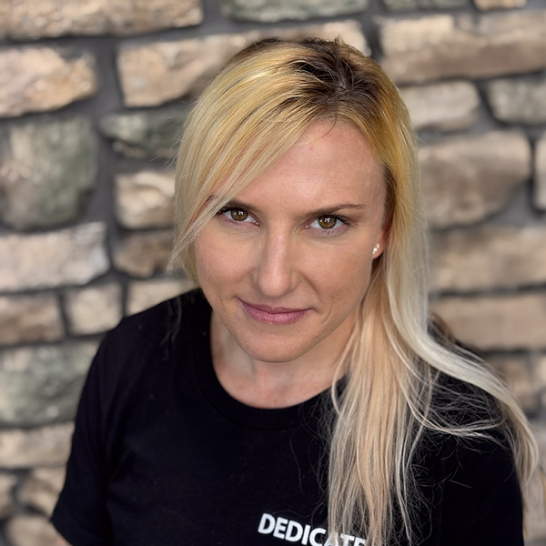 Stephanie Cook, Plant Operations Director at Vitalia Highland Heights, looking at the camera in a professional headshot with long blonde hair swept to one side, a black top, and a stacked stone wall background.