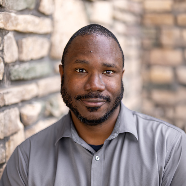 Fred Kope, Business Office Director at Vitalia Highland Heights, looking at the camera in a professional headshot with short dark hair, a trimmed beard, a gray collared shirt, and a softly blurred stone wall background.